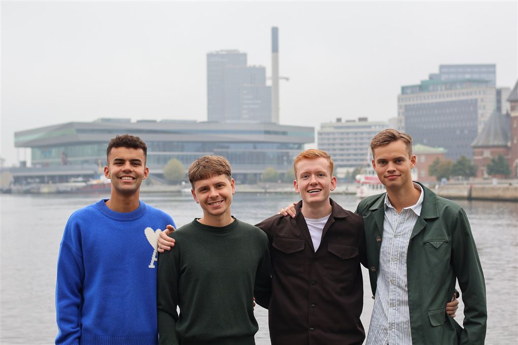 4 unge mænd smiler ved en havnefront